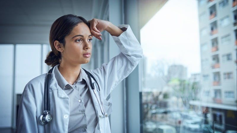 Young, tired-looking female doctor looking out window physician resident residency burn out burned out